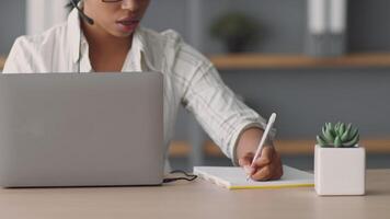A woman is effectively teaching from home, using a laptop and notepad. She interacts with students remotely, demonstrating modern online education techniques. video