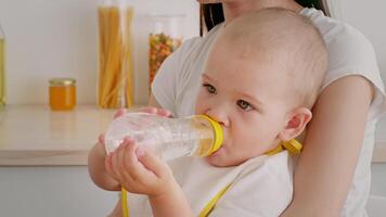 A young child sits comfortably on a caregiver's lap, happily drinking from a bottle in a cozy indoor setting. They share a moment together in a nurturing environment. video