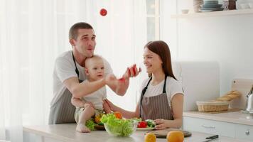 A toddler sits on the counter while parents prepare fresh vegetables in a bright, cozy kitchen. The family enjoys quality time together, fostering care and connection. video