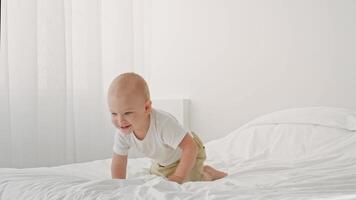 A cheerful toddler with short hair crawls playfully on a soft bed, surrounded by a bright, airy room. Sunlight filters through sheer curtains, creating a warm atmosphere. video