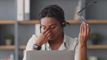 uma focado africano americano mulher é acionado dentro controlo remoto ensino. ela desgasta uma fone de ouvido enquanto segurando óculos e é usando uma computador portátil, refletindo dela comprometimento para conectados Educação e tutoria. video