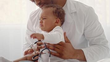 A young African American child is held by a caregiver indoors, showing signs of distress during a health checkup. The room is bright and airy, creating a nurturing atmosphere. video
