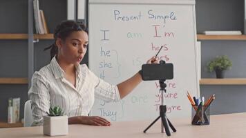 A dedicated woman teaches English grammar concepts to her students during an online session. The environment is set up for effective remote learning with a laptop and teaching materials. video