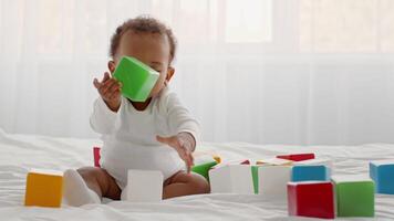 African American toddler sits on a soft surface, engaged in stacking and arranging colorful blocks. Sunlight streams in through the window, creating a cheerful atmosphere for playtime. video