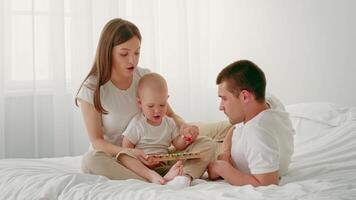 A young child engages with colorful toys as both parents sit beside him on a soft bed. The room is filled with natural light, creating a warm and nurturing atmosphere. video