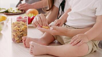 A young child sits on a parent's lap, captivated by vibrant pasta shapes. The kitchen is colorful, with fresh vegetables and ingredients visible, creating a nurturing environment for learning. video