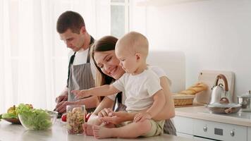 A joyful family engages in meal preparation at home. The smiling mother plays with her toddler while the father chops vegetables, creating a warm and loving atmosphere. video