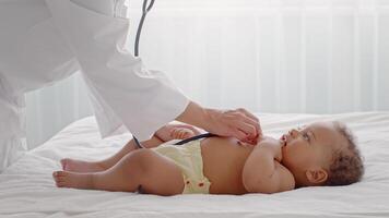 A caring medical professional examines a toddler indoors. The child lies comfortably on a bed, showing curiosity and calmness during the check-up, fostering a serene atmosphere of trust. video