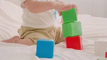 A young child joyfully stacks brightly colored blocks on a soft surface. The toddler focuses intently on balancing the blocks while playing in a cozy indoor setting during playtime. video