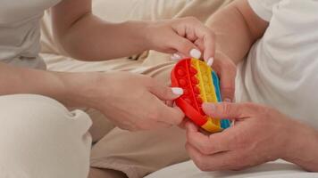 A toddler and a caregiver are enjoying an interactive play session together on a soft surface. The child explores a colorful toy, showcasing curiosity and bonding through hand motions. video