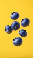 Six blueberries fresh organic fruit floating on air and vertical solid yellow background photo