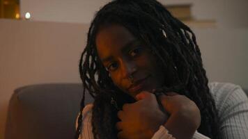 Close-up portrait of a young African American woman looking down, then lifting her gaze to the camera with a gentle, subtle smile in a calm and intimate setting. video