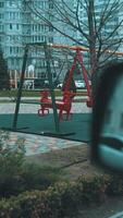 Swing set swaying in the wind on a deserted playground, surrounded by apartment buildings. Tranquil and cinematic urban scene video