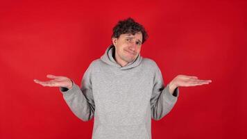 retrato do confuso homem encolhendo os ombros ombros dentro perplexidade, duvidando e sentindo-me incerto, não conhecer responder. interior estúdio tiro isolado em vermelho fundo. conceito - ter não ideia, talvez. video