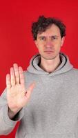 serious man raises hand, palm forward, showing in front sign stop, ban, rejected gesture. Isolated red background studio shot. Concept - avoid, danger disapproval negative emotions must not impossible video