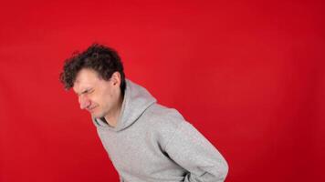 young adult curly man suffers from attacks abdominal pain, stomach, indigestion, poisoning, nausea, heartburn, bloating, colic. Isolated red background, studio shot. concept poor nutrition, fast food video