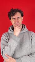 Young adult curly serious thoughtful man holds chin, rubs fingers, looks around, solves problem in head. Can't make up his mind. Isolated red background studio shot. Concept - brainstorming, choice. video
