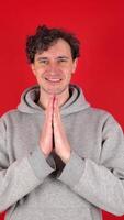 Portrait happy man laughing and smiling, showing thank you, namaste gesture, grateful for smth. He folded hands, palms facing each other in front. standing isolated over red background studio shot. video
