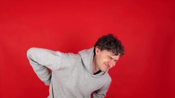man suffers from back pain, sports injury, muscle spasm. who has lower back pain side problems after training, jogging. back flank ache problem after exercise. Isolated red background, studio shot. video