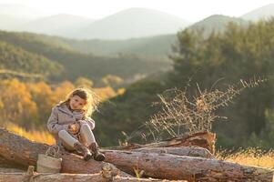 In a quiet mountain meadow, a child in casual clothes sits on logs and bites into a red apple at dawn. photo