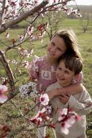 Under the canopy of pink almond blossoms, the boy and girl stand together, smiling widely, their bond radiating love and joy photo