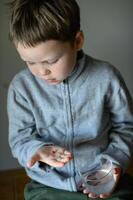 A little boy with a serious expression holds a pill in his hand. photo