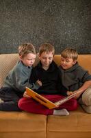 An older boy gently turns the pages of a book while his younger brothers sit beside him, eager to hear more. photo