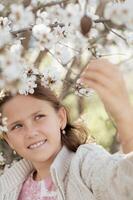 A portrait of a young girl in a white dress, smiling warmly as the almond flowers bloom around her, their soft petals falling gently in the breeze photo