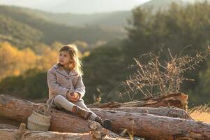 Blonde child in a rustic setting enjoys a fresh apple while sitting on wooden logs during early morning light. photo