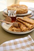 Freshly made pancakes with honey dripping from a honey dipper sit on a countryside table, creating a cozy summer breakfast scene photo