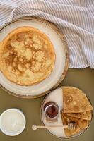 A stack of golden pancakes is drizzled with honey, with a dollop of sour cream on the side, beautifully presented on a rustic plate. photo