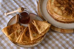 Warm pancakes drizzled with honey. A cozy breakfast scene featuring a stack of pancakes topped with golden honey, with a honey dipper resting beside them. photo
