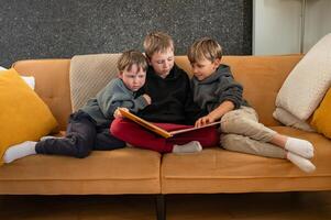 Three boys sit closely on a couch the oldest reads aloud while the younger ones follow along with curiosity. photo