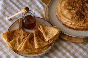 Homemade crepes with honey on a bright breakfast table. Thin, delicate crepes are arranged next to a small jar of honey and a honey dipper, creating a cozy morning atmosphere. photo