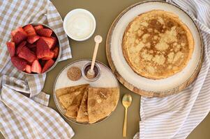 Crispy-edged pancakes with a honey dipper resting on top, paired with a bowl of sour cream and fresh strawberries, creating a perfect balance of flavors photo