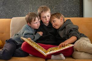 A cozy scene of three boys sitting on a couch, with the eldest reading a book and the younger ones listening intently photo