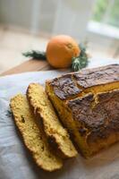 A golden-brown orange cake rests on a ceramic plate, its surface lightly drizzled with glaze, while fresh orange slices add a burst of vibrant color. photo