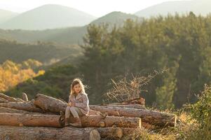 In the early hours of the day, a girl with light hair eats an apple while sitting on a pile of logs in nature. photo