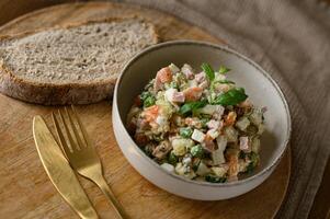 A plate of traditional Olivier salad served with a slice of dark sourdough bread, accompanied by a fork and knife. photo
