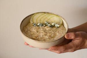 A bowl of creamy oatmeal topped with sliced pear, crumbled Gorgonzola, and a drizzle of honey, styled as a food photo. photo