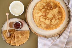 A stack of warm pancakes with a honey dipper resting on top, paired with rich sour cream, shot in a cozy, inviting atmosphere. photo