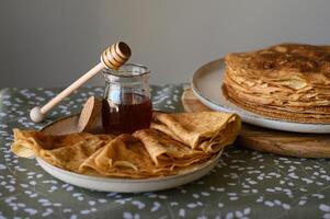 Rustic pancake with a honey jar and dripping honey dipper. A soft pancake rests on a homey tablecloth, while golden honey drizzles from a dipper into a nearby jar. photo