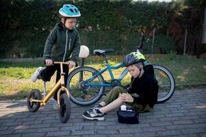 Two small cyclists take a break while one puts a plaster on his scraped knee after a minor fall. photo
