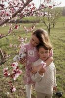 With big smiles on their faces, a boy and girl hold each other under the vibrant pink blossoms of an almond tree, creating a picture of springtime happiness. photo