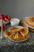 Cozy pancake breakfast with sweet toppings. A warm, inviting table with a stack of pancakes, drizzled honey, fresh strawberries, and a bowl of sour cream. photo