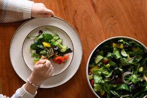 A vibrant fresh salad with colorful vegetables is served on a plate, with hands holding a fork, ready to take a bite. photo