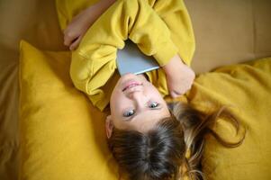 Relaxing on the sofa, girl smiles while using her tablet. photo