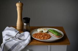 A protein-packed breakfast dish with velvety avocado on toast, rich tomato beans, and a golden egg, served on a stylish plate. photo