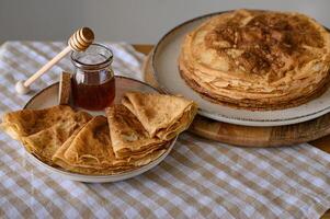 Golden pancakes with honey on a light tablecloth. A stack of warm, golden-brown pancakes served with a jar of honey and a wooden honey dipper on a soft, light tablecloth. photo