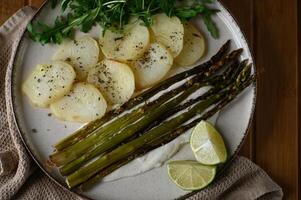 A top-down food shot of asparagus on a creamy bed, plated with golden potatoes, crisp arugula, and a refreshing lime wedge. photo